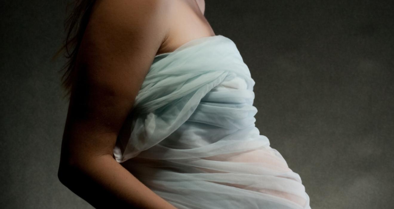 picture of a pregnant woman wrapped in light blue fabric looking at her bump