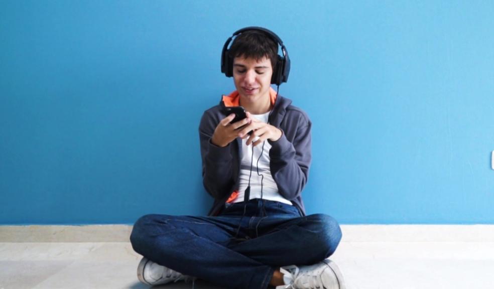 picture of a teenager with autism sat on his phone with headphones on