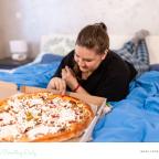 picture of a student eating pizza in bed