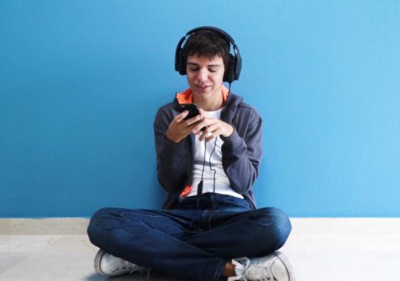 picture of a teenager with autism sat on his phone with headphones on