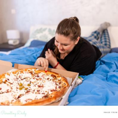 picture of a student eating pizza in bed